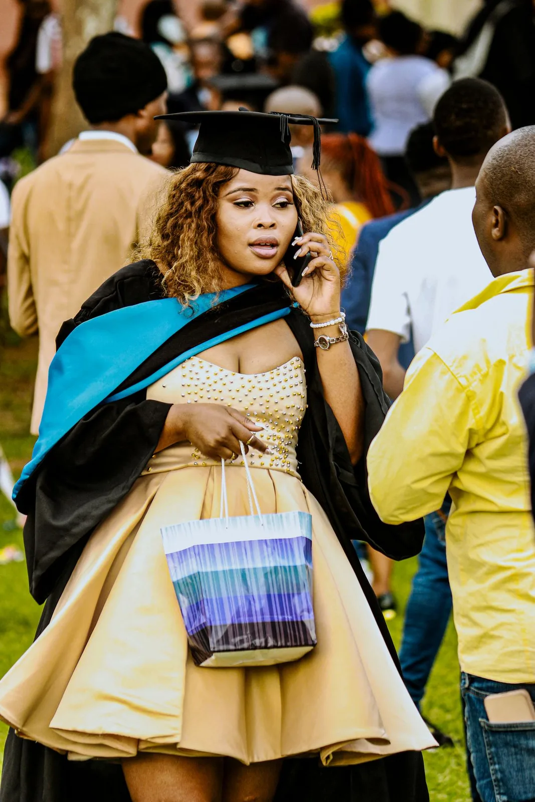 A graduate celebrating in cap and gown at an outdoor graduation ceremony