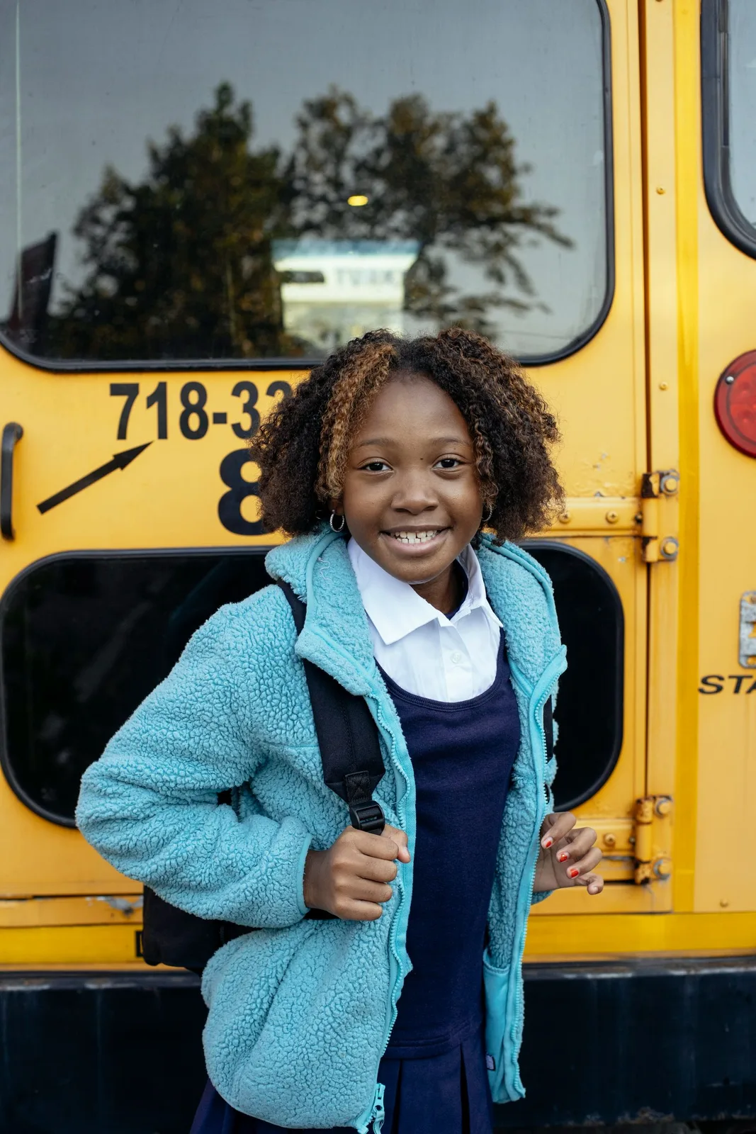A student standing beside the school bus, backpack in hand